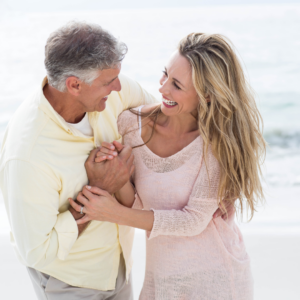 Man with grey hair in light yellow shirt and women with long blonde hair in pink sweater on the beach